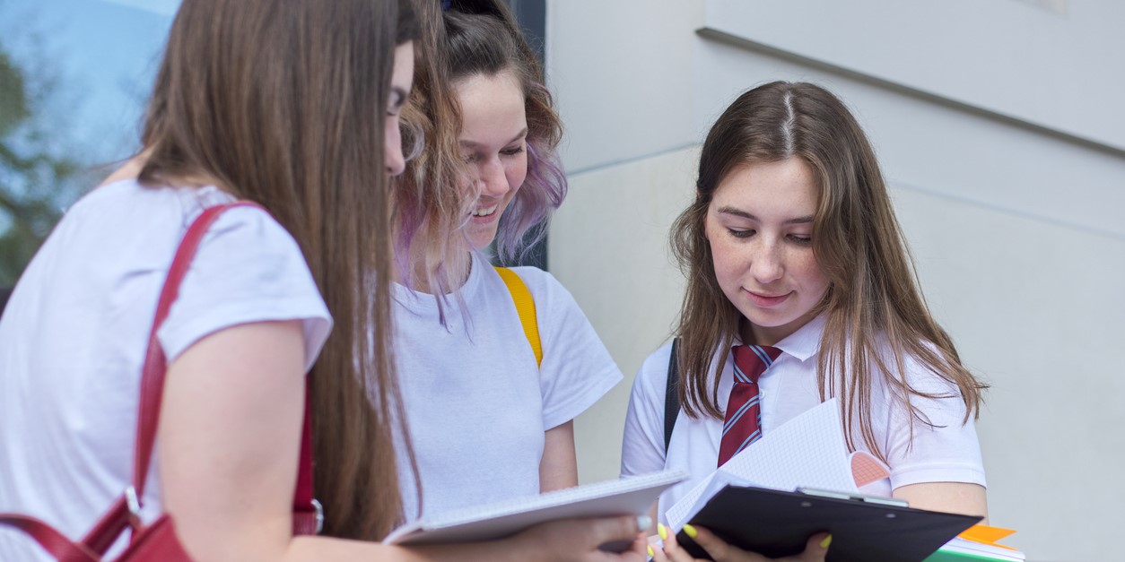 Three teenagers stand with backpacks and books outdoors