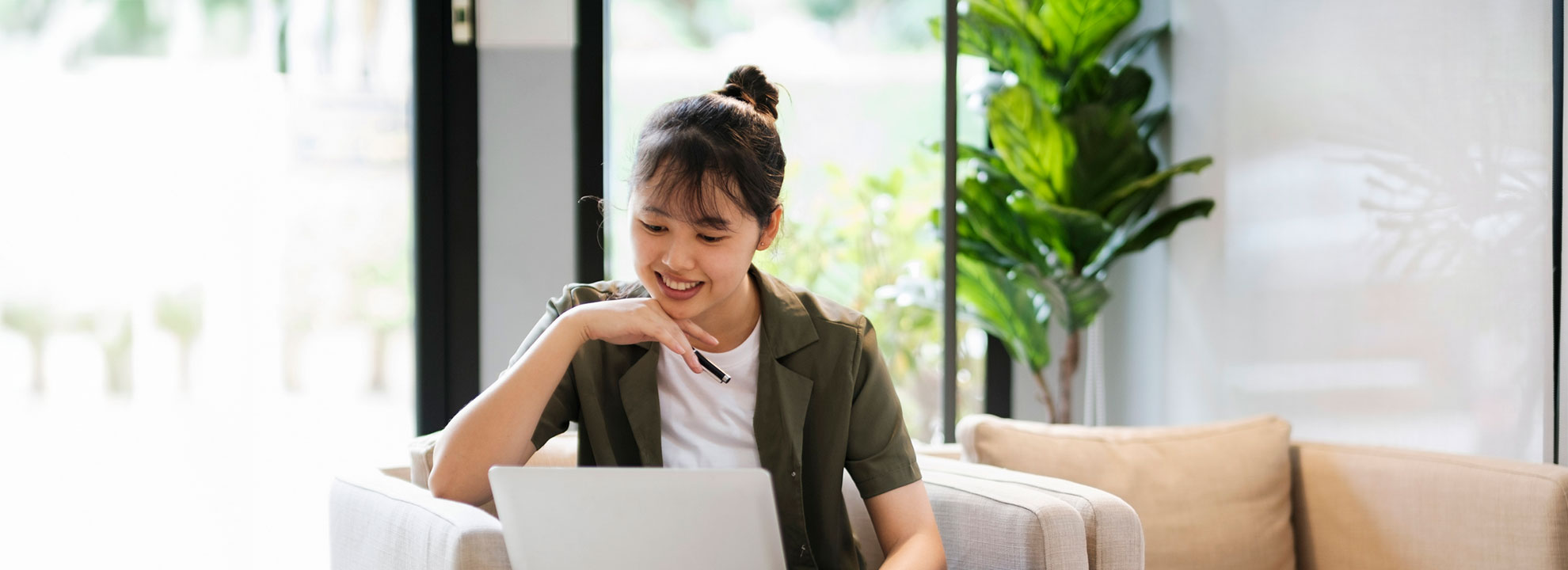 A woman sitting on a couch in a sunny room looking at a computer screen.
