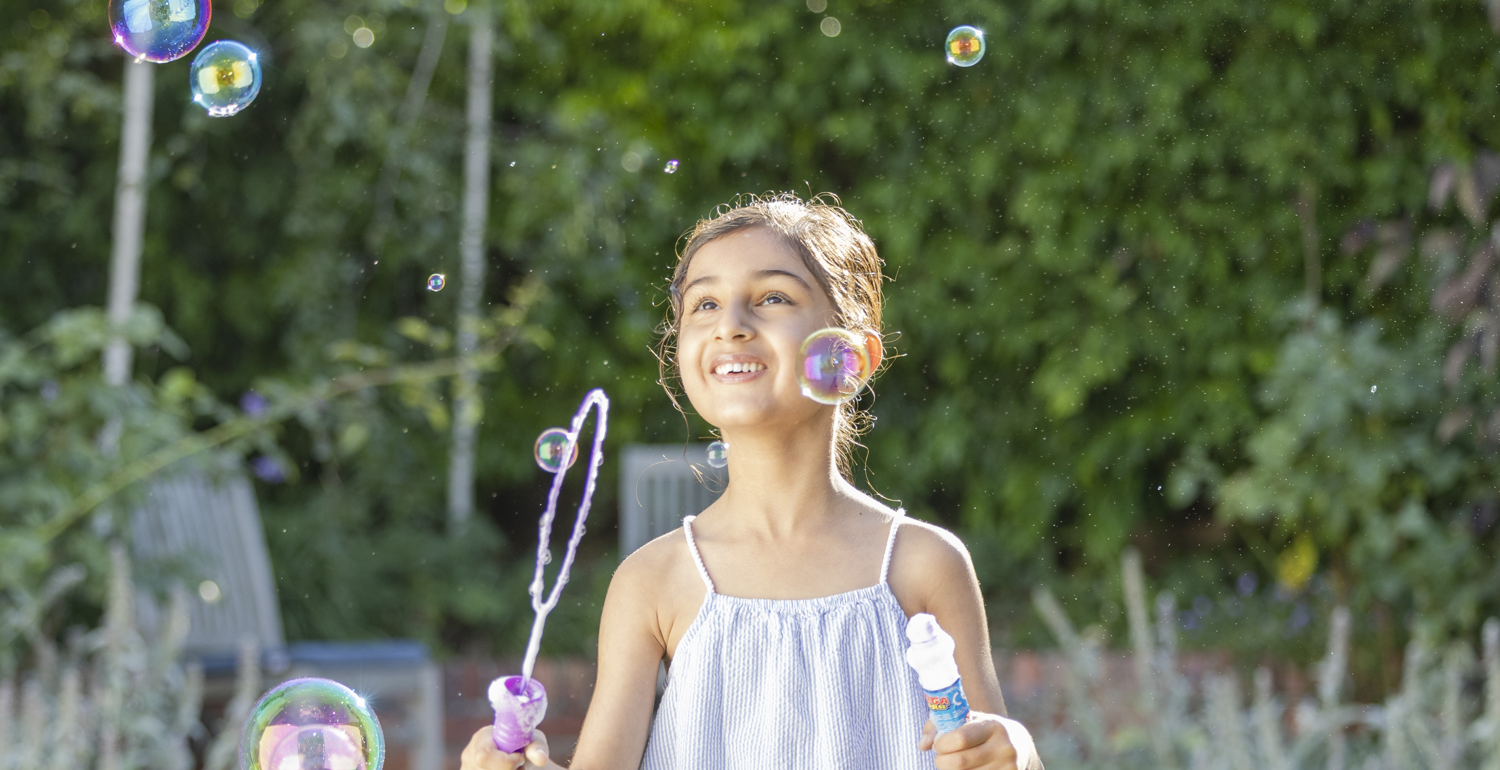 Young girl holding bubble wand surrounded by bubbles and looking up at them