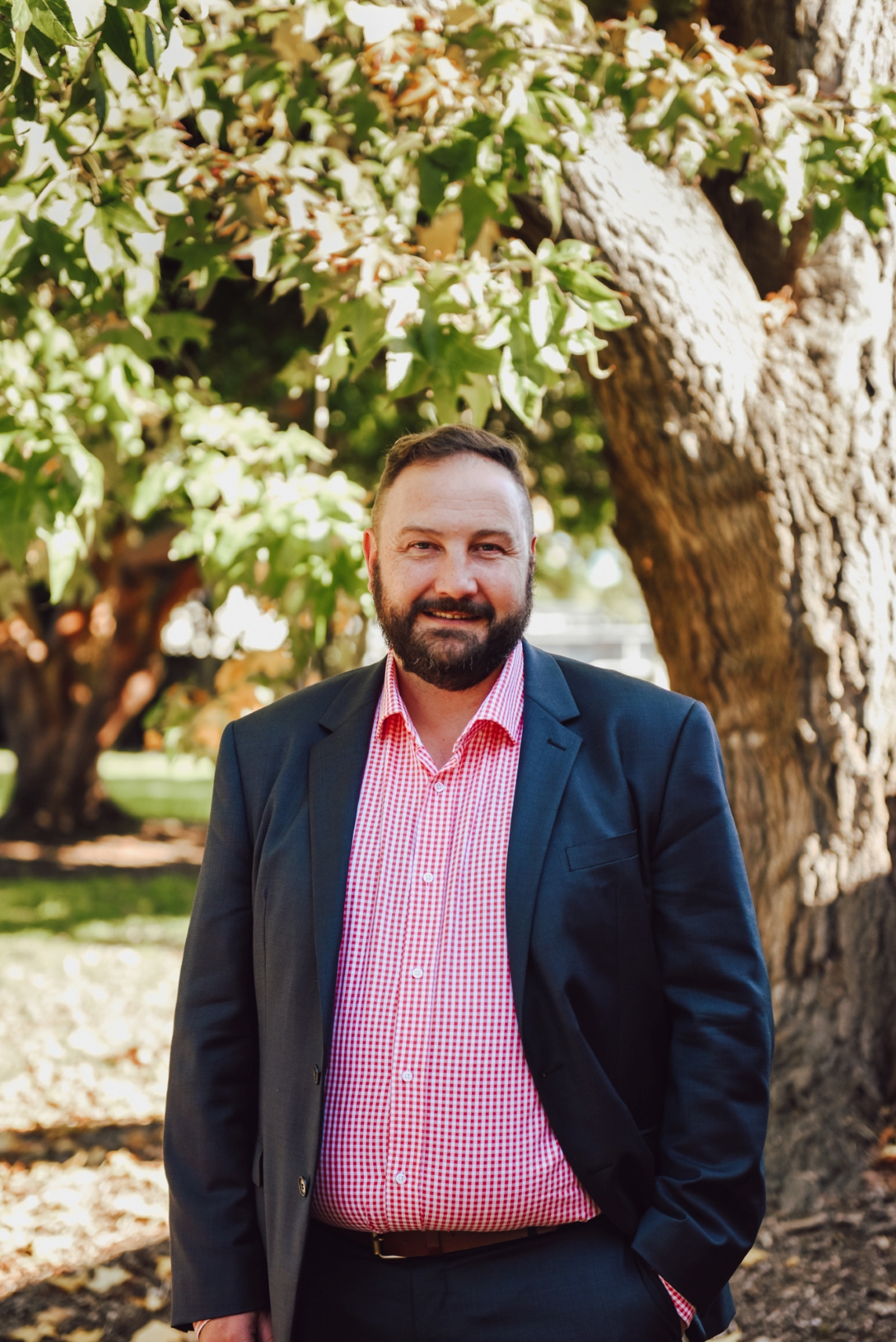 A man standing in front of a tree, wearing a suit