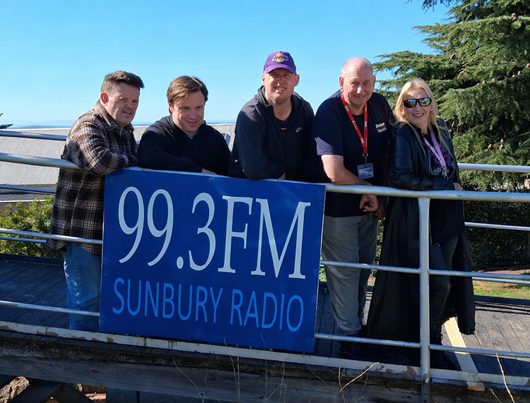 Members of the Sunbury Radio community standing in front of the station's banner, saying "99.3FM Sunbury Radio"