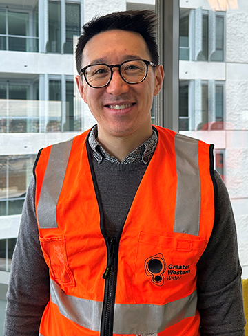 David has dark hair and glasses and is wearing a bright orange vest.