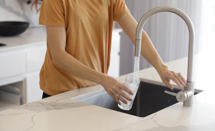 A person filling a glass with water from a kitchen tap