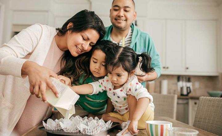 A photograph of a mother, father and two young children making cupcakes
