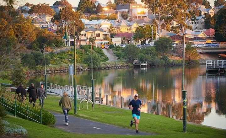 A photograph showing people walking and exercising in a park adjacent to a small lake. 