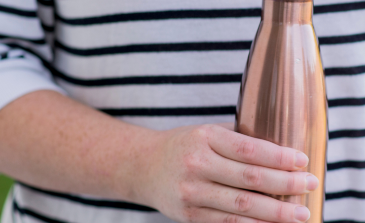 A person in striped jumper holding a rust coloured water bottle