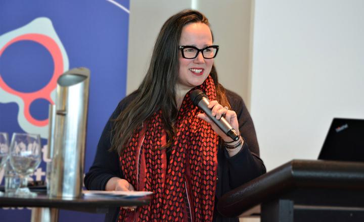 A woman holds a microphone and speaks at a lectern.