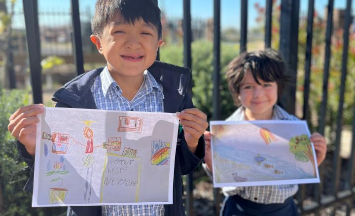 Two happy school students hold posters they have drawn. 