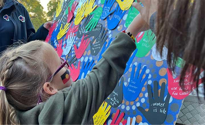 A young girl attaching her commitment to Country paper hand to the board