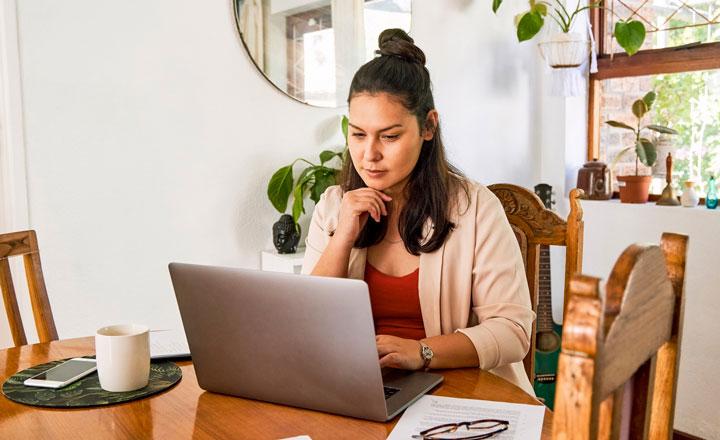 A woman sitting at a table looking at a laptop computer