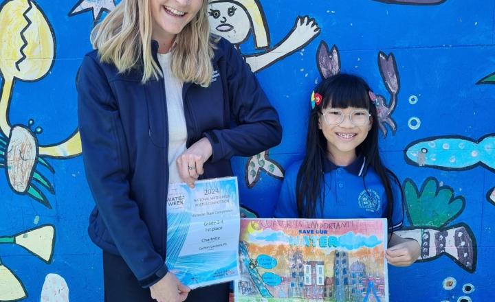 A woman standing with a young girl holding a colourful poster.