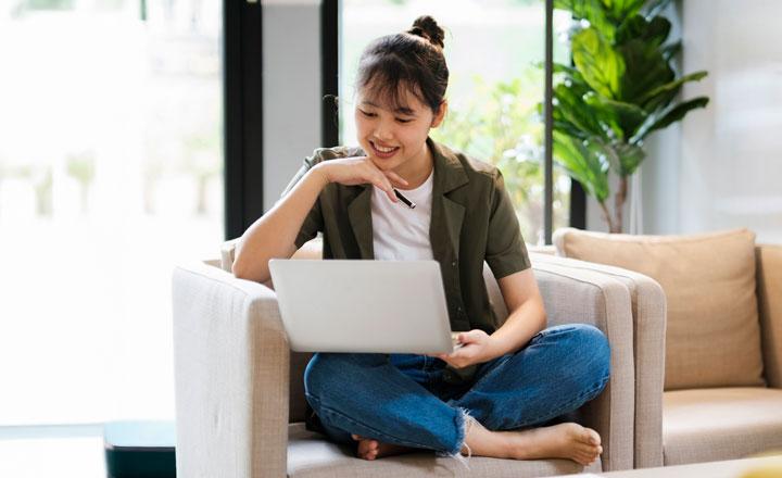 A woman sitting on a couch in a sunny room looking at a computer screen.