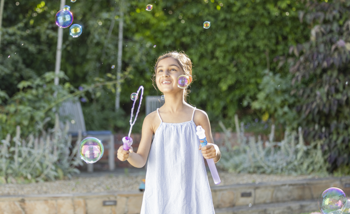 Young person holding bubble wand surrounded by bubbles and looking up