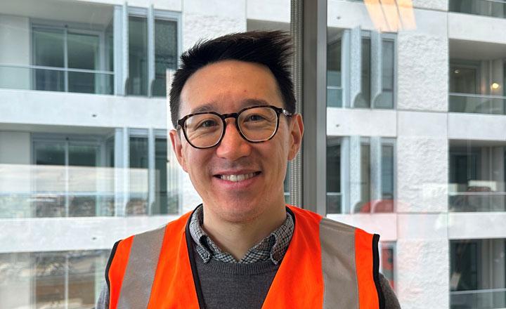 David has dark hair and glasses and is wearing a bright orange vest.