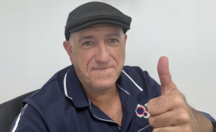 Headshot of Richard wearing a dark flat cap and a navy-blue shirt gives a thumbs-up while sitting indoors. The shirt has the GWW logo near the collar.