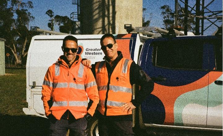Two men in PPE gear standing next to a GWW branded vehicle