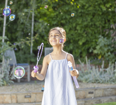 Young person holding bubble wand surrounded by bubbles and looking up